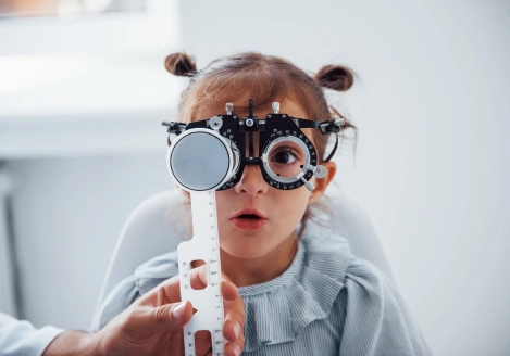 Niña pequeña con cabello recogido en dos coletas, usando un foróptero durante un examen de la vista.